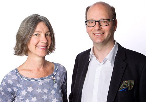 Zwei lächelnde Erwachsene posieren vor weißem Hintergrund für ein professionelles Porträtfoto.